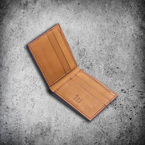 IM™ Luxurious open bifold wallet showing cognac leather interior with 6 card slots, embossed logo, and distinctive purple painted edges against a navy exterior.
